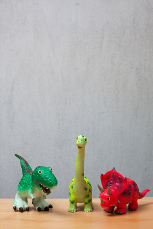 Three dinosaurs toys standing on a wooden floor.の写真素材