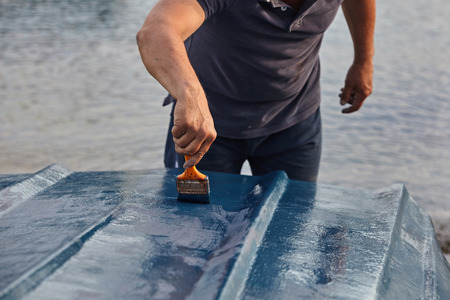 Man painting boat.Closeup view of hand holding a paintbrush with blue color.の写真素材