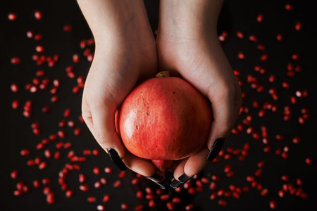 hands holding a pomegranate fruite on black background full of seeds.の写真素材