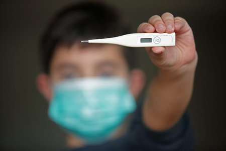 kid wearing a medical mask and holding a thermometer.