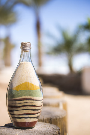 bottle with colored sand standing on a logの写真素材