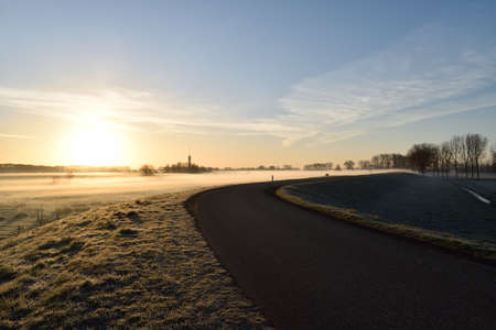 A winding Dutch road under a rising morning sun which is creating ground frost close to Oss, Netherlandsの写真素材