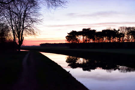 A stunning sunrise sky overlooking the still water of a canal and casting reflections in the waterの写真素材
