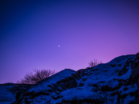 Beautiful winter landscape with snow covered mountains and a crescent moonの写真素材
