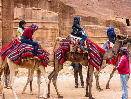 PETRA, JORDAN: Group of tourists riding camels, getting ready for the trip, beside are the drivers - bedouins. Camels covered with bright national coverlet, Petra (Rose City)のeditorial素材