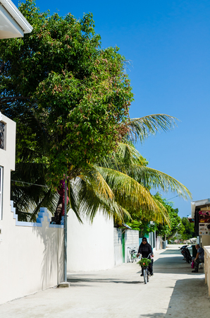 Huraa, Maldives - November 20, 2017: woman riding a bicycle on the narrow street of a small tropical island with a backdrop of palm trees and a bright blue sky, Kaafu Atoll, Kuda Huraa Island, Maldives.のeditorial素材