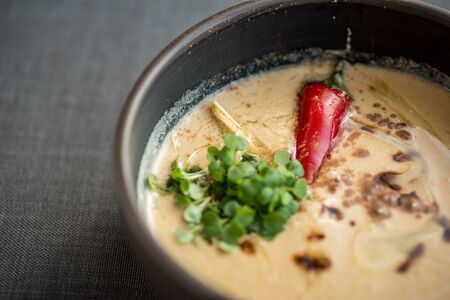 Vegetable cream soup with a whole red chili pepper in a stone bowlの写真素材