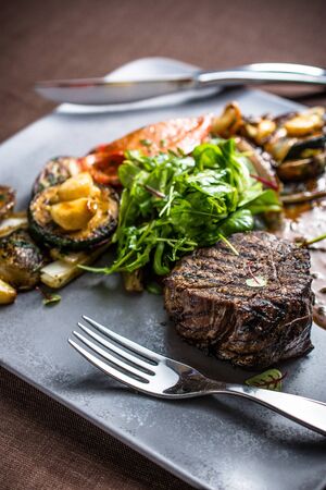 Grilled beef meat with grilled vegetables, gravy sauce and fresh green leavesの写真素材