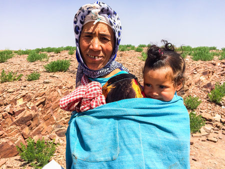Zaida, Morocco - April 10, 2015. Berbere woman in traditional clothes wearing cute girl on her back