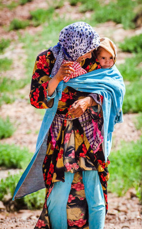 Zaida, Morocco - April 10, 2015. Berbere woman in traditional clothes wearing cute girl on her back