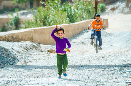 Aouli, Morocco - April 10, 2015. Cute moroccan berber girl running and waving toward to the tourists followed by the boy on the bikeのeditorial素材