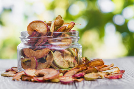 Homemade apple chips. Dried fruit. Healthy snack in a glass jar and on a wooden surface with green...