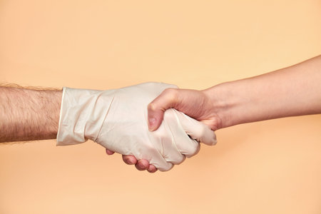 Two person handshake on a beige background. One person wearing in rubber gloves for protection...
