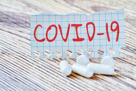 Inscription COVID-19 near the pills on the wooden background. Concept of protection from Coronavirus. Closeup, selective focusの写真素材
