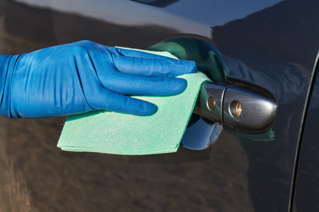 Hand of man in blue protective glove is wiping with a cloth an exterior handle of car door. Coronavirus or Covid-19 protection