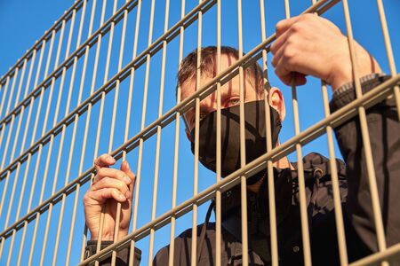 A man in a black protective face mask near the metal fence. Quarantine. Coronavirus concept. A man wearing protective mask.の写真素材