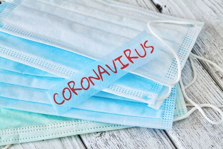 Some medical masks on wooden background with Inscription Coronavirus. Concept of protection from Covid-19. Closeup.の写真素材