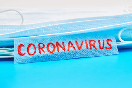 Stack of medical masks on the blue background with Inscription Coronavirus. Concept of protection...