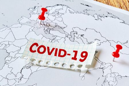 A part of world map with red pushpins in Italy and China where is covid-19 epidemic and the inscription COVID-19 on a piece of paper. Concept of the spread of the virusの写真素材