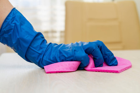 A human hand in a protective glove disinfects the table with a cleaning cloth for viruses prevention