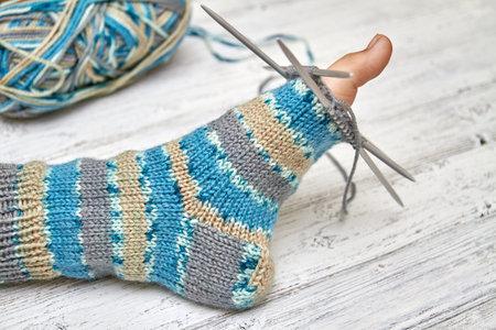 Try on sock on a baby foot while knitting. Light wooden background, selective focus