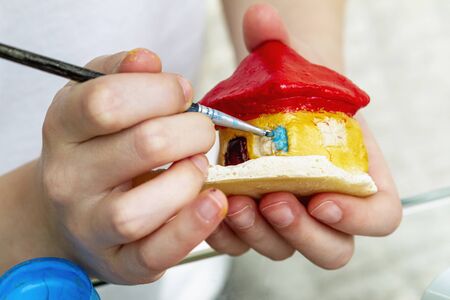 Little girl paints the house from clay or salty dough with acrylic paints. Education concept.の写真素材