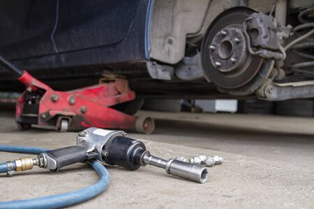 Pneumatic wrench tool on the asphalt and a car jack for lift up the body and changing the tire. Car without wheelの写真素材