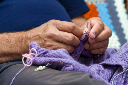 Closeup of elderly man knitting a purple sweater. Knitting like hobbies handmade.