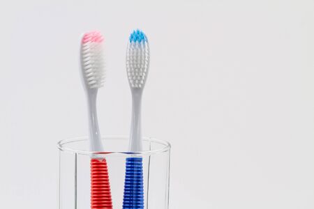 New red and blue plastic toothbrushes in the transparent glass. Bathroom wall. Light blue background. Closeup, copy space.の写真素材