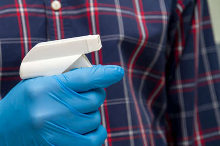 A man in blue protective glove holds a bottle with a disinfectant. Protection from bacteria and viruses.の写真素材