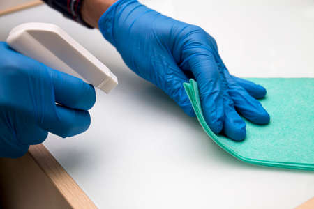 A man in blue protective gloves disinfects the surfaces in the store using a rag and spray disinfectant. Protection from bacteria and viruses.の写真素材