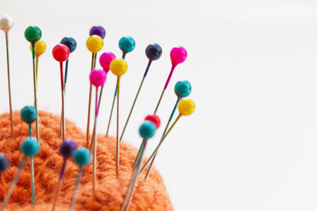 Multicolored sewing pins in the orange pin cushion on light background. Closeup, selective focus
