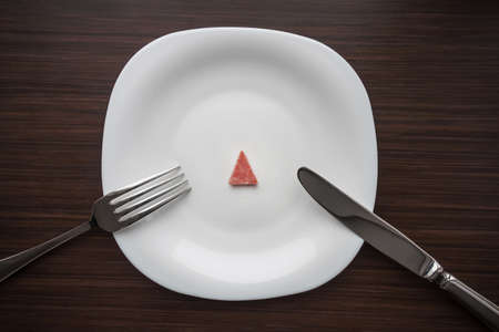 A small piece of sausage on the white plate with knife and fork. Dark backgroundの写真素材