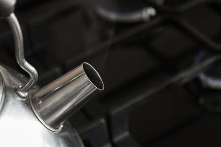 A part of the steel tea kettle with boiling water on black gas stove with burning gas burnersの写真素材