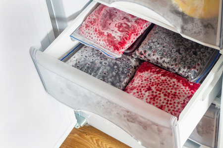 Frozen berries in transparent plastic bags in the freezer. Open deep freeze filled with frozen Red...