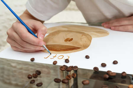 Coffee drawings. Girl draws a coffee cup using coffee instead of paintsの写真素材