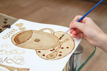 Coffee drawings. Girl draws a coffee cup using coffee instead of paintsの写真素材