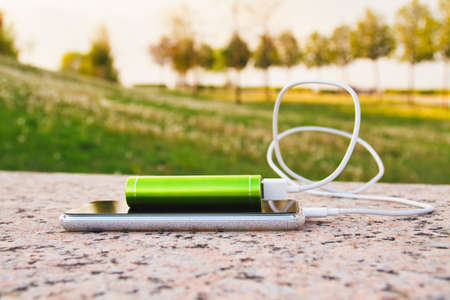 Smartphone and external power bank lie on the granite surface in the park while chargingの写真素材
