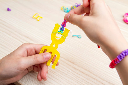 Rubber Band Weaving. Knitting rubber bands with loom knit. Hands of girl weaving wristband of rubber bands.の写真素材