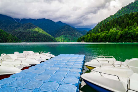 Jetty with white catamarans on the Ritsa Lake in Abkhazia. Mountain lake with green pine forest hills at the shoreの写真素材