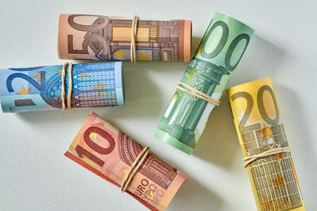 Ten, twenty, fifty and one and two hundred Euro bill rolled up as a tubule lies on the light background. Euro banknotes details in a macro shot. Closeup, selective focusの写真素材