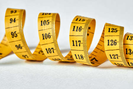 Yellow color centimeter with black figures for measurement of length and width on a white background. Measuring tape of the tailor for you design. Closeup, selective focusの写真素材