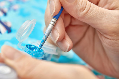 Woman draws with a brush painting by numbers on canvas. Picture by numbers. Drawing on canvas. Creative hobby. Painting for beginners. The concept of a hobby. Closeup, selective focusの写真素材