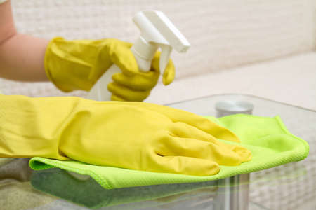 Hands in protective gloves with rag and spray are cleaning the glass coffee tableの写真素材