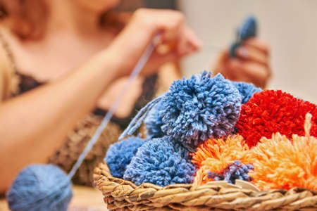 A basket with handmade pompons. The process of making pompons from threads by woman on the background.の写真素材