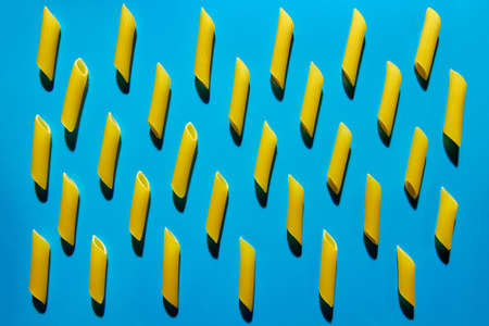 Yellow pasta on a blue background in hard light. Flat lay from macaroniの写真素材