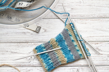 Sock in the process of knitting on light wooden background. Closeup, selective focus