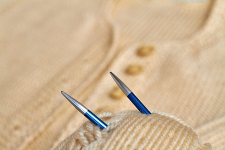 Knitting needles in a beige ball on the background of a knitted product. Closeup, selective focus