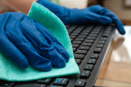 Girl's hand in blue protective glove cleans keyboard with a cloth for prevention coronavirus,...