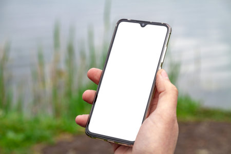 A man uses his smartphone on the shore of a pond